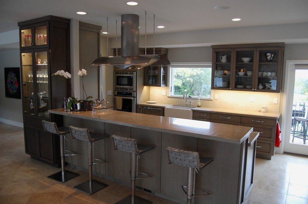 Open concept kitchen - mid-sized transitional galley travertine floor open concept kitchen idea in Orange County with a farmhouse sink, shaker cabinets, gray cabinets, limestone countertops, beige backsplash, stone tile backsplash, stainless steel appliances and a peninsula