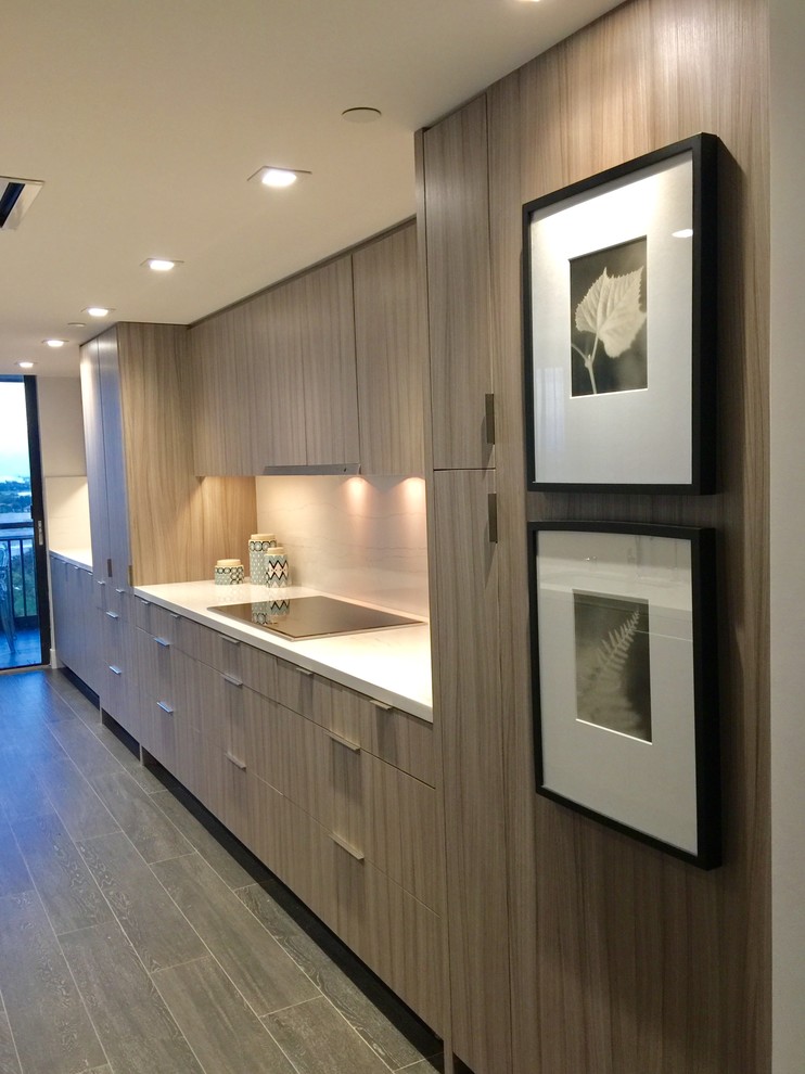 This is an example of a modern galley kitchen pantry in Miami with an undermount sink, flat-panel cabinets, medium wood cabinets, quartz benchtops, white splashback, stone slab splashback, stainless steel appliances, porcelain floors, black floor and white benchtop.