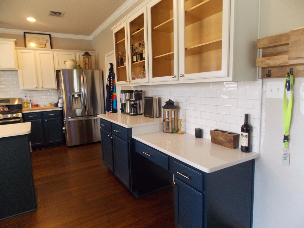This is an example of a mid-sized country l-shaped eat-in kitchen in Austin with a farmhouse sink, flat-panel cabinets, blue cabinets, quartz benchtops, white splashback, subway tile splashback, stainless steel appliances, medium hardwood floors and a peninsula.