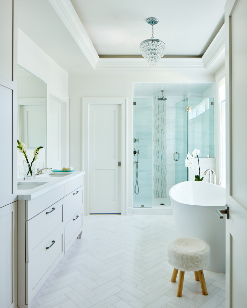 Photo of a large transitional master bathroom in New York with shaker cabinets, white cabinets, a freestanding tub, marble floors, an undermount sink, engineered quartz benchtops, white floor and white benchtops.