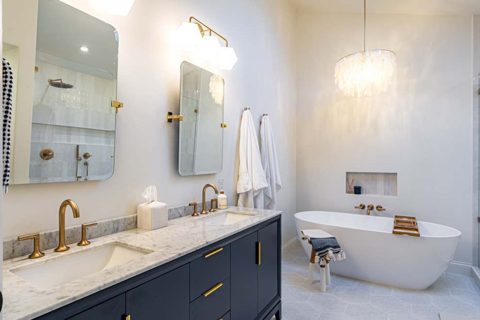 Photo of a large modern ensuite bathroom in Orange County with blue cabinets, a freestanding bath, beige walls, porcelain flooring, a built-in sink, marble worktops, grey floors, grey worktops, double sinks, a built in vanity unit, flat-panel cabinets, white tiles, ceramic tiles, a wallpapered ceiling, wallpapered walls, a shower bench, an open shower and a double shower.