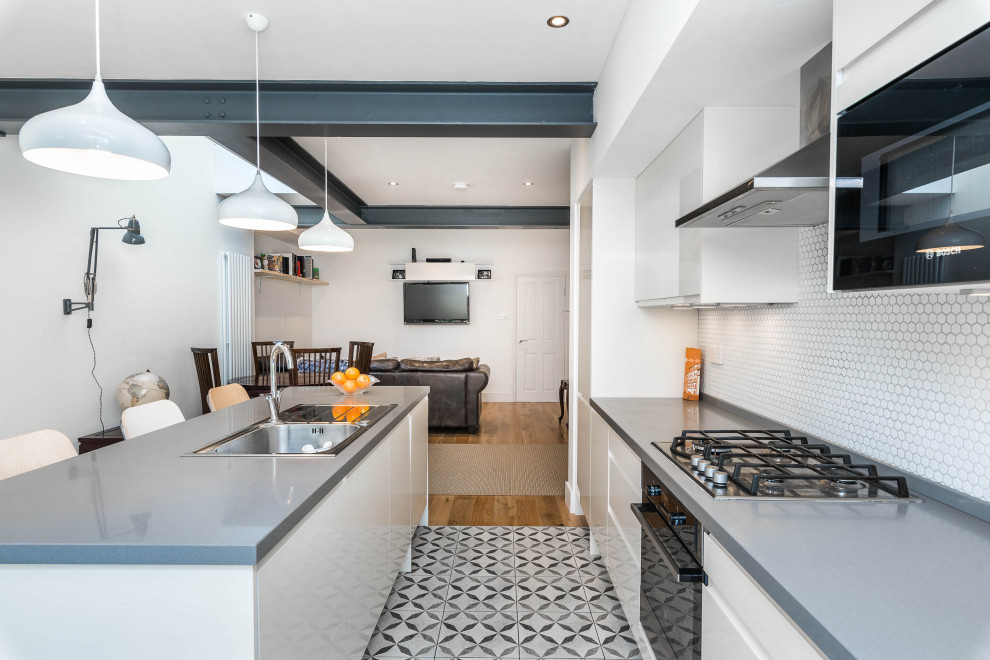 Design ideas for a medium sized traditional grey and white galley open plan kitchen in London with a built-in sink, flat-panel cabinets, beige cabinets, granite worktops, white splashback, mosaic tiled splashback, integrated appliances, ceramic flooring, an island, grey floors and grey worktops.