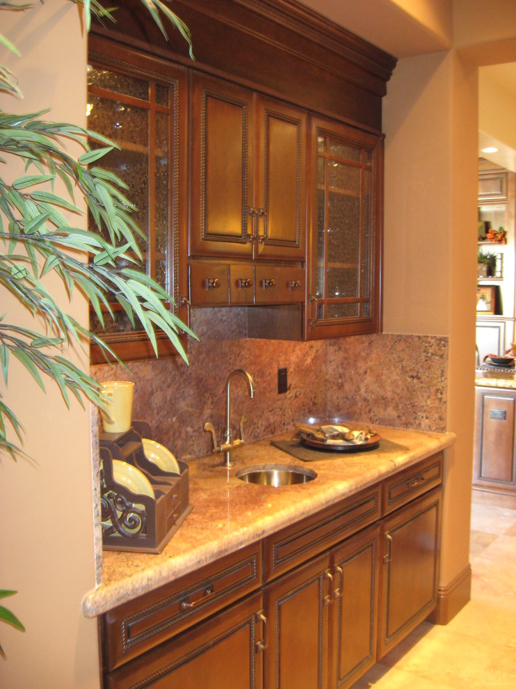 Photo of a large traditional galley wet bar in Las Vegas with an undermount sink, raised-panel cabinets, medium wood cabinets, granite benchtops, stone slab splashback and travertine floors.