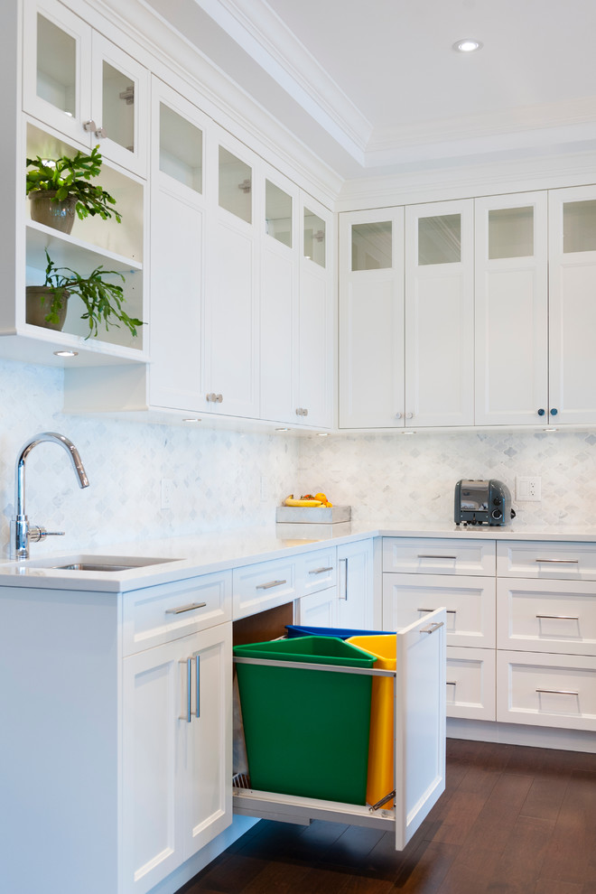 Photo of an expansive transitional l-shaped open plan kitchen in Vancouver with an undermount sink, shaker cabinets, white cabinets, marble benchtops, white splashback, stone tile splashback, white appliances, medium hardwood floors and with island.