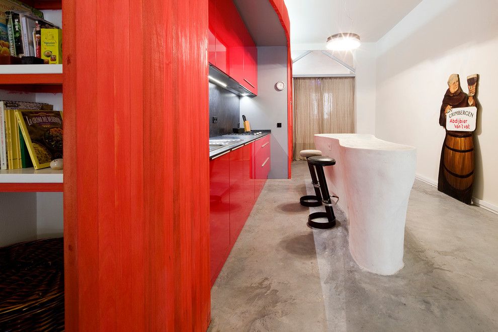 Mid-sized eclectic single-wall open plan kitchen in Madrid with a single-bowl sink, flat-panel cabinets, red cabinets, concrete floors and with island.