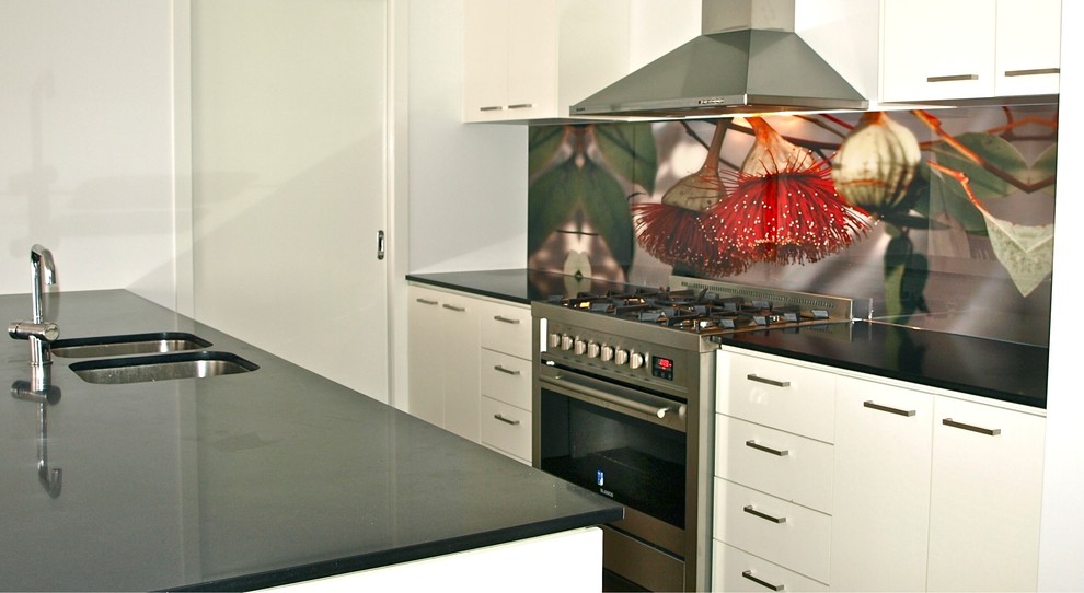 Inspiration for a mid-sized contemporary single-wall eat-in kitchen in Melbourne with a drop-in sink, flat-panel cabinets, white cabinets, quartz benchtops, multi-coloured splashback, glass sheet splashback, stainless steel appliances, dark hardwood floors, with island, brown floor and black benchtop.