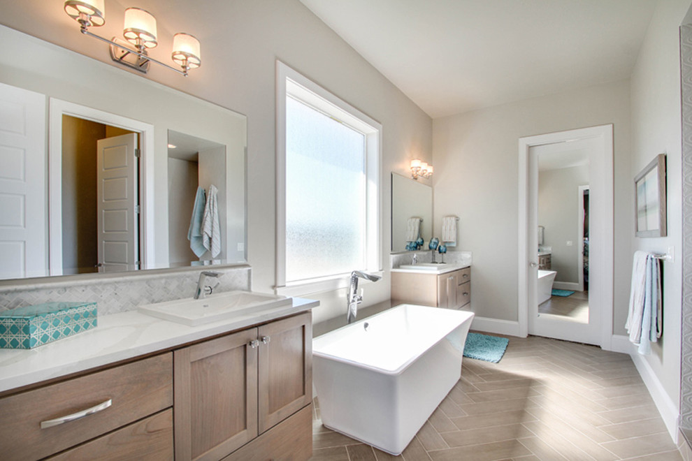 Mid-sized transitional master bathroom in Boise with shaker cabinets, medium wood cabinets, a freestanding tub, gray tile, marble, grey walls, porcelain floors, a drop-in sink, engineered quartz benchtops, beige floor and white benchtops.