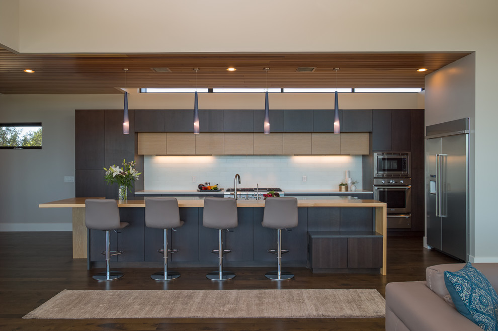 Inspiration for a contemporary l-shaped open plan kitchen in Austin with flat-panel cabinets, dark wood cabinets, white splashback, stainless steel appliances, dark hardwood floors, with island, brown floor and brown benchtop.