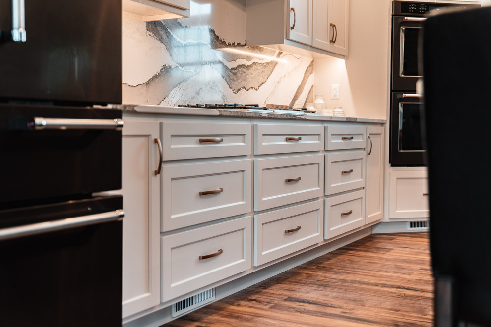 Open concept kitchen - large transitional l-shaped medium tone wood floor and brown floor open concept kitchen idea with an undermount sink, flat-panel cabinets, white cabinets, quartz countertops, multicolored backsplash, quartz backsplash, black appliances, an island and multicolored countertops
