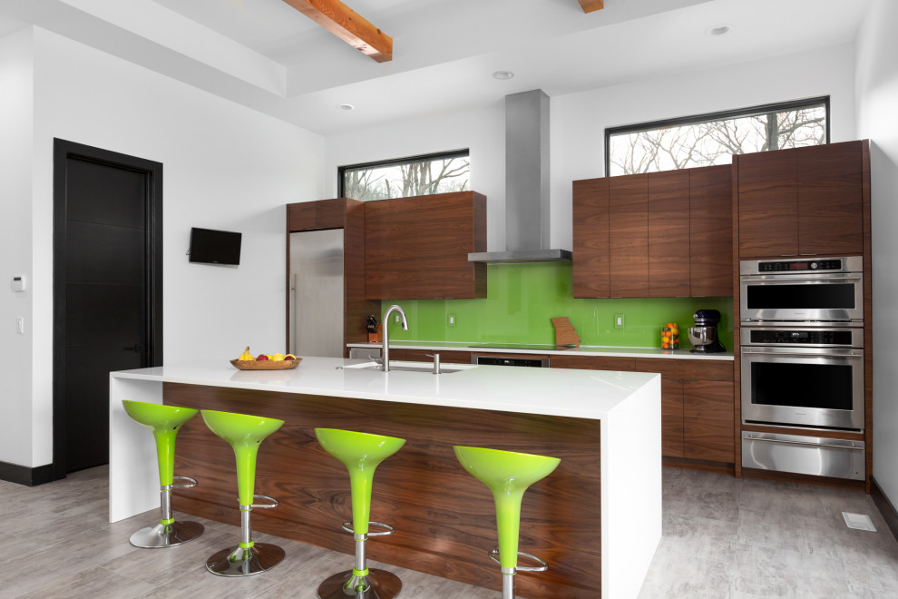 Design ideas for a mid-sized midcentury galley eat-in kitchen in St Louis with an undermount sink, flat-panel cabinets, medium wood cabinets, quartzite benchtops, green splashback, glass sheet splashback, stainless steel appliances, vinyl floors, with island, grey floor, white benchtop and exposed beam.