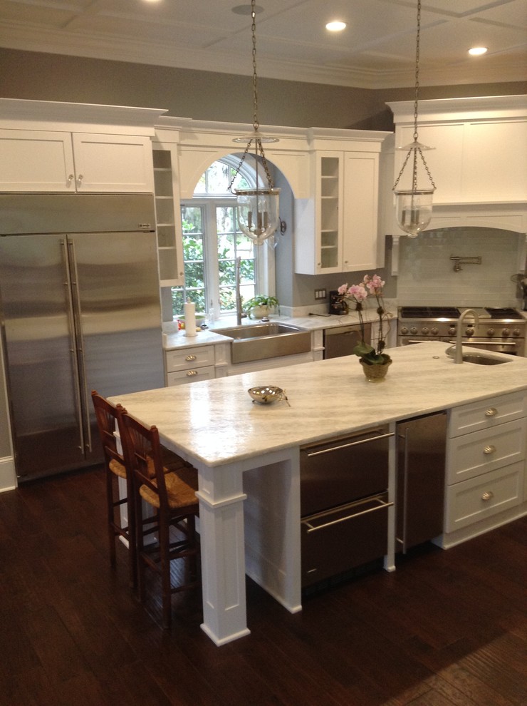 Mid-sized traditional l-shaped open plan kitchen in Jacksonville with a farmhouse sink, shaker cabinets, white cabinets, quartzite benchtops, white splashback, subway tile splashback, stainless steel appliances, medium hardwood floors and with island.