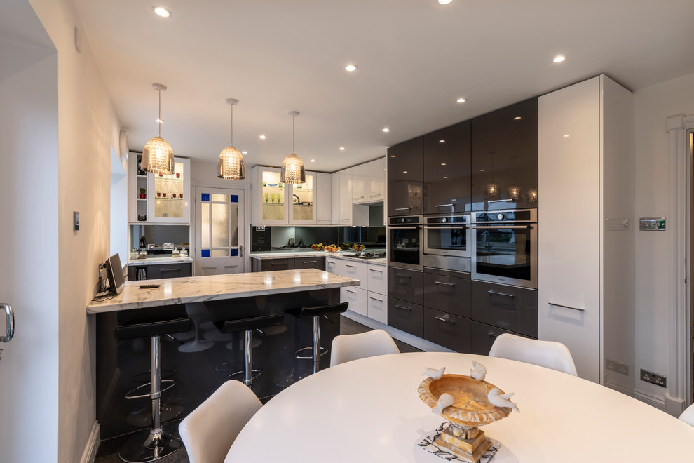 Mid-sized contemporary eat-in kitchen in Cheshire with flat-panel cabinets, laminate benchtops, grey splashback, glass sheet splashback, black appliances, vinyl floors, grey floor and white benchtop.