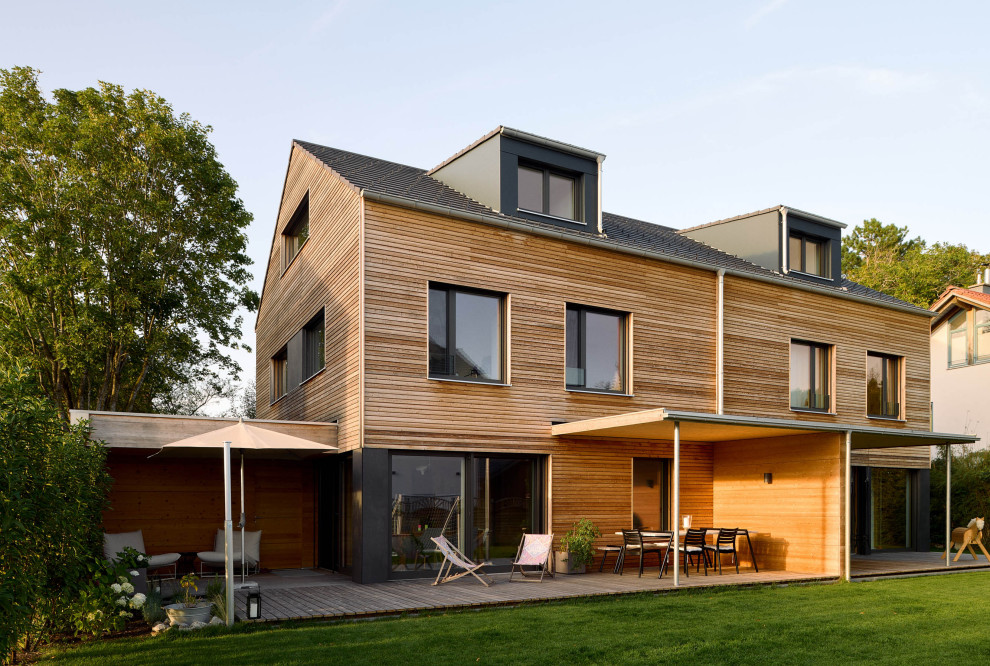 Esempio della facciata di una casa bifamiliare marrone contemporanea a due piani con rivestimento in legno, tetto a capanna, copertura in tegole, tetto nero e pannelli sovrapposti