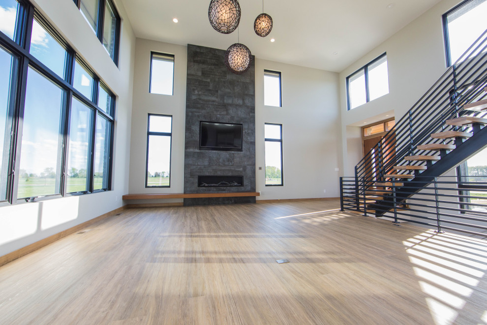 This is an example of a large modern open plan living room in Indianapolis with beige walls, medium hardwood flooring, a standard fireplace, a tiled fireplace surround, a wall mounted tv, brown floors and a vaulted ceiling.