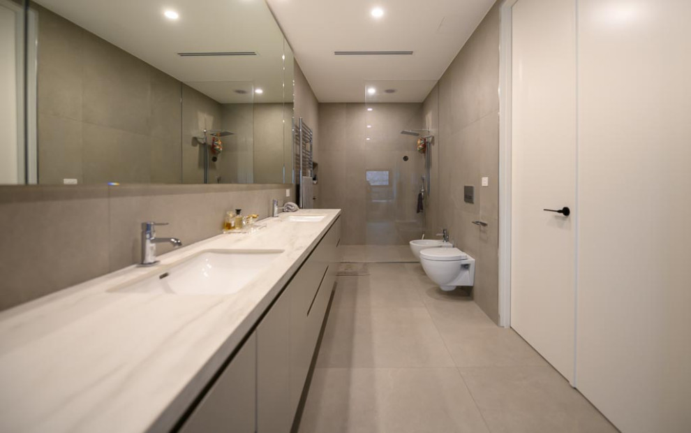 Cette image montre une grande salle de bain avec un placard à porte plane, des portes de placard grises, une baignoire indépendante, un espace douche bain, WC suspendus, un carrelage gris, des carreaux de porcelaine, un mur gris, un sol en carrelage de porcelaine, un lavabo encastré, un sol gris, meuble double vasque, meuble-lavabo suspendu et un plan de toilette en quartz modifié.