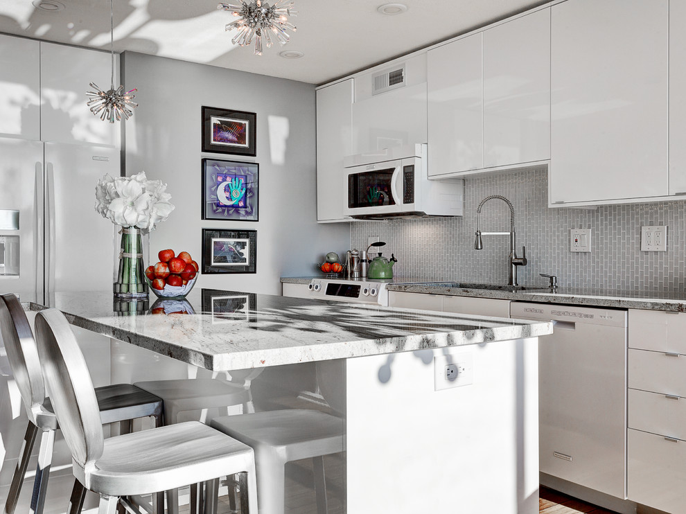 Inspiration for a mid-sized contemporary galley kitchen in Los Angeles with flat-panel cabinets, white cabinets, marble benchtops, grey splashback, glass tile splashback, white appliances and with island.