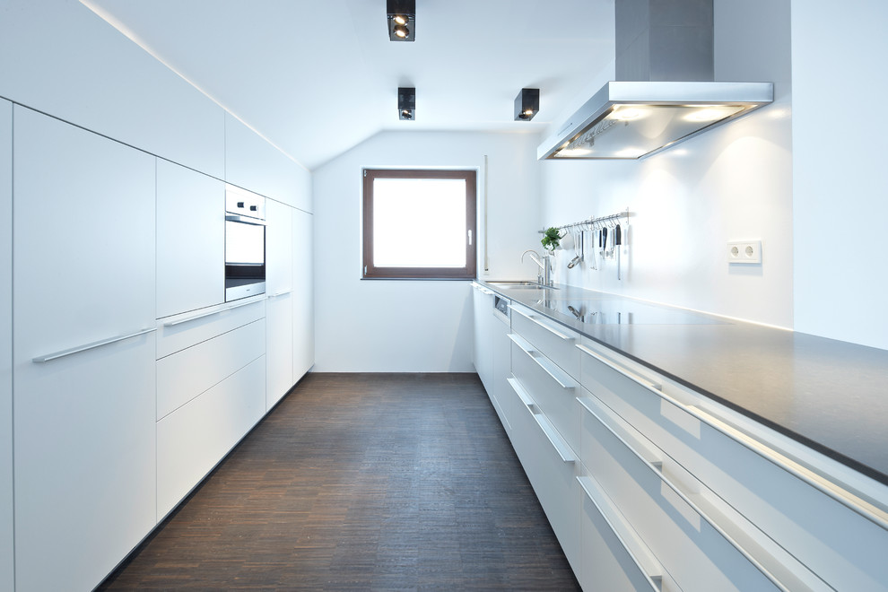 Large contemporary galley separate kitchen in Stuttgart with an undermount sink, flat-panel cabinets, white cabinets, stainless steel appliances, no island, white splashback and dark hardwood floors.