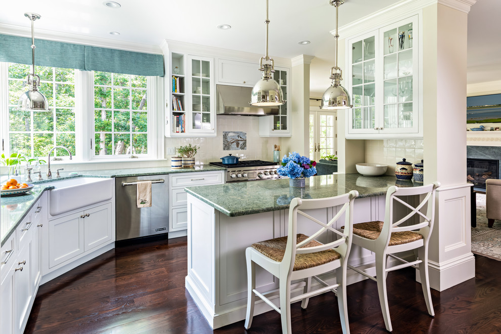 Inspiration for a beach style l-shaped open plan kitchen in Boston with a farmhouse sink, glass-front cabinets, white cabinets, white splashback, stainless steel appliances, dark hardwood floors, a peninsula, brown floor and blue benchtop.