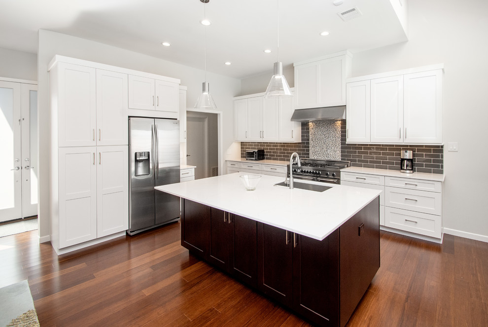 Inspiration for a large transitional single-wall open plan kitchen in Dallas with an undermount sink, flat-panel cabinets, white cabinets, quartz benchtops, grey splashback, glass tile splashback, stainless steel appliances, bamboo floors, with island, brown floor and white benchtop.