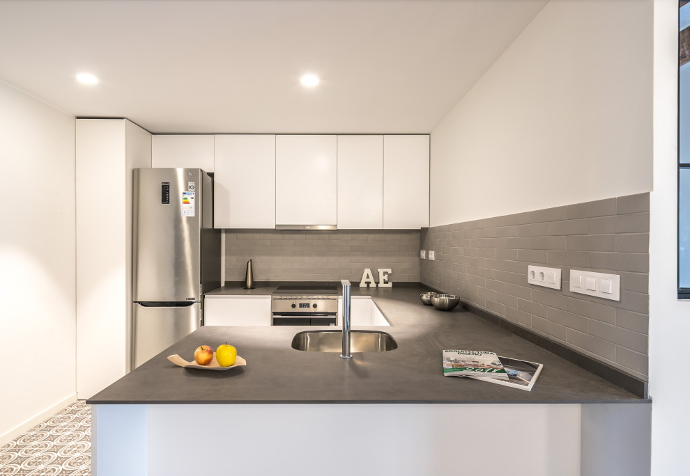 Photo of a small modern grey and white u-shaped open plan kitchen in Barcelona with a submerged sink, white cabinets, grey splashback, metal splashback, stainless steel appliances, ceramic flooring, a breakfast bar, white floors and grey worktops.