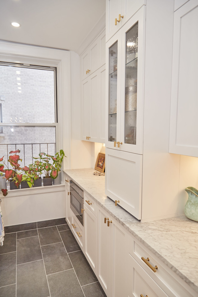 Transitional galley kitchen in New York with a farmhouse sink, shaker cabinets, white cabinets, quartz benchtops, white splashback, ceramic splashback, stainless steel appliances, cement tiles, grey floor and grey benchtop.