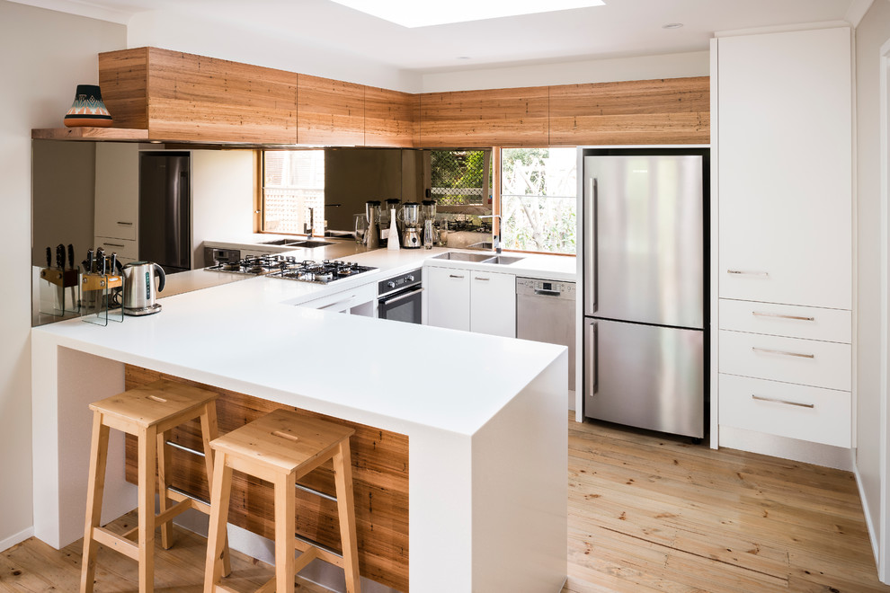 Small contemporary u-shaped eat-in kitchen in Melbourne with a double-bowl sink, white cabinets, solid surface benchtops, mirror splashback, stainless steel appliances and no island.