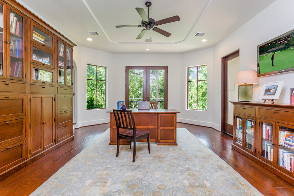 Photo of a large mediterranean home office in Houston with a library, white walls, medium hardwood floors, a freestanding desk and brown floor.