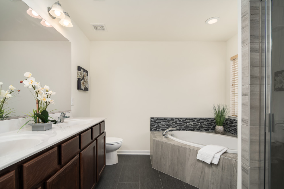 Inspiration for a mid-sized traditional master bathroom in DC Metro with flat-panel cabinets, dark wood cabinets, a corner tub, a corner shower, a one-piece toilet, gray tile, glass tile, beige walls, cement tiles, a console sink, marble benchtops, black floor, a hinged shower door and white benchtops.