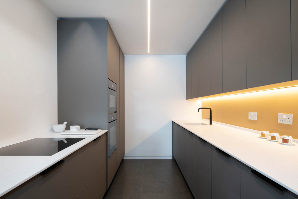 This is an example of a modern galley kitchen in London with a double-bowl sink, flat-panel cabinets, grey cabinets, yellow splashback, no island, grey floor and white benchtop.