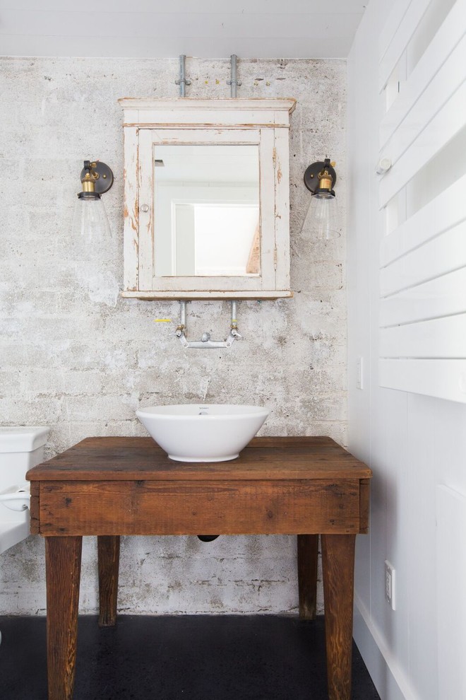 Photo of a country bathroom in Santa Barbara with furniture-like cabinets, white walls, concrete floors, a vessel sink, wood benchtops and black floor.