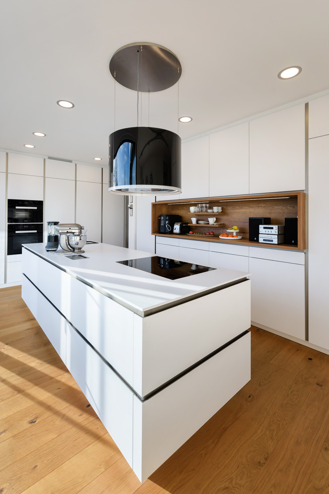 Photo of a mid-sized contemporary l-shaped open plan kitchen in Stuttgart with an integrated sink, flat-panel cabinets, white cabinets, solid surface benchtops, white splashback, timber splashback, black appliances, painted wood floors, with island and brown floor.
