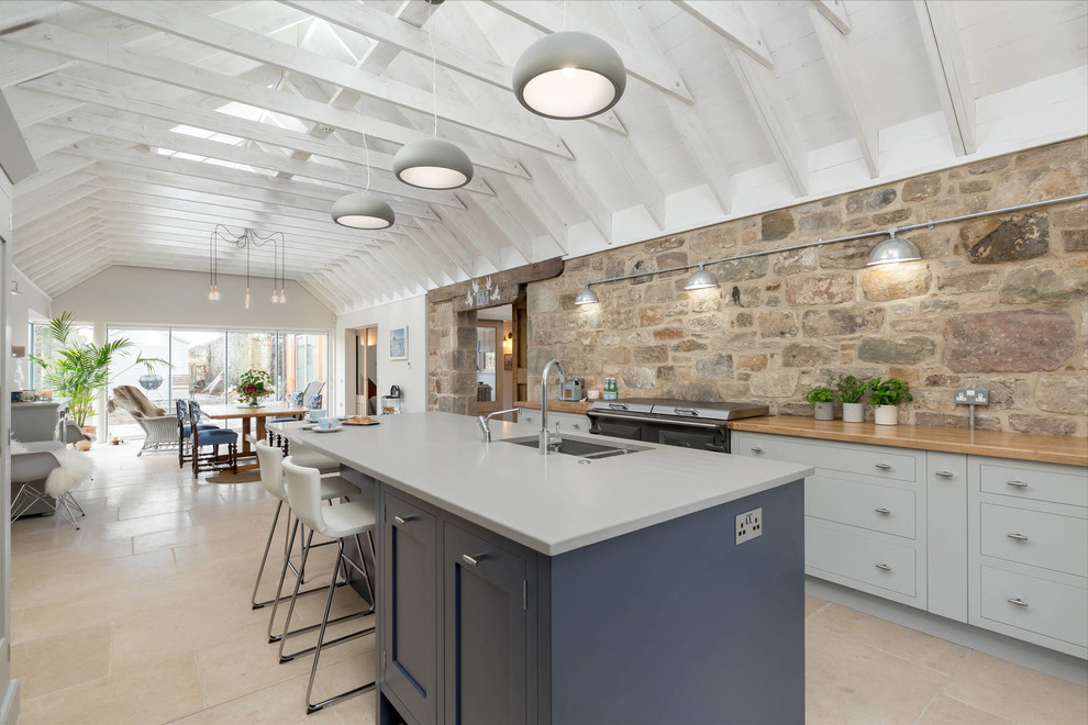 This is an example of a large country eat-in kitchen in Edinburgh with flat-panel cabinets, grey cabinets, quartzite benchtops, stainless steel appliances, travertine floors, with island and an undermount sink.