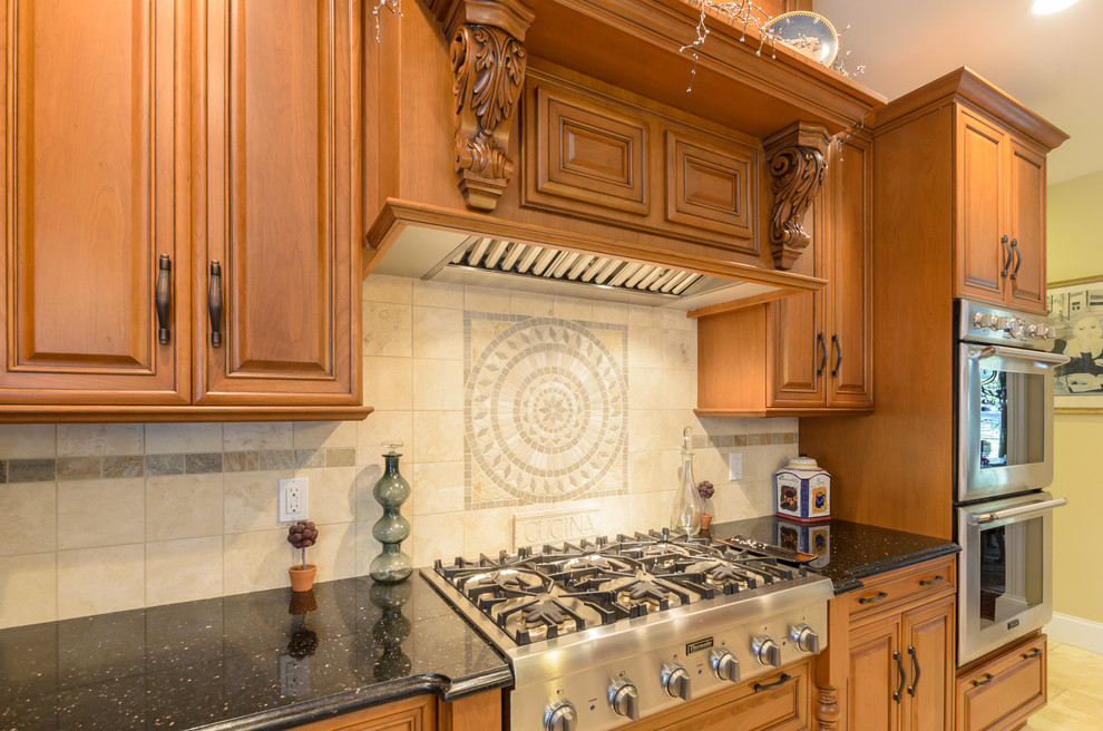 This is an example of a traditional l-shaped eat-in kitchen in Boston with an undermount sink, raised-panel cabinets, brown cabinets, granite benchtops, beige splashback and stainless steel appliances.