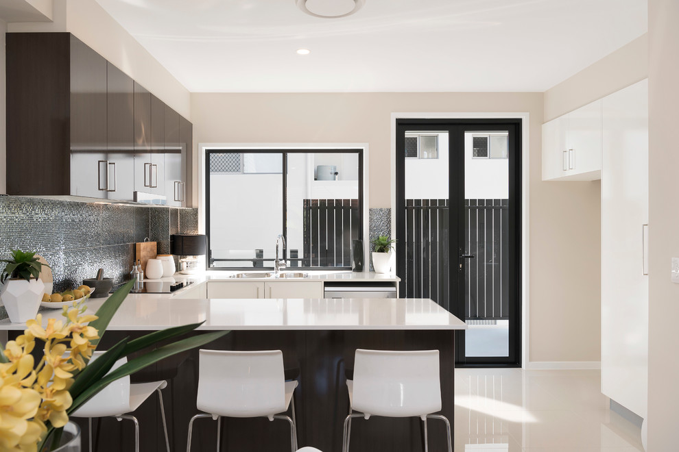 Photo of a small modern u-shaped open plan kitchen in Brisbane with a double-bowl sink, flat-panel cabinets, quartz benchtops, metallic splashback, ceramic splashback, stainless steel appliances, porcelain floors, a peninsula and white cabinets.