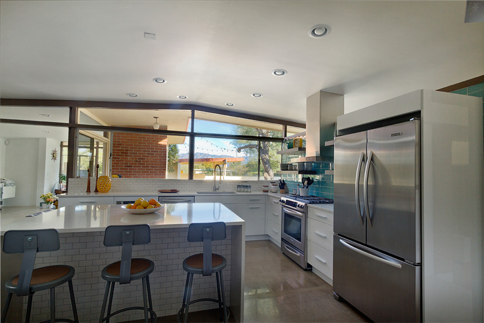 Design ideas for a mid-sized midcentury l-shaped open plan kitchen in Phoenix with an undermount sink, flat-panel cabinets, white cabinets, quartz benchtops, blue splashback, glass tile splashback, stainless steel appliances, concrete floors and with island.