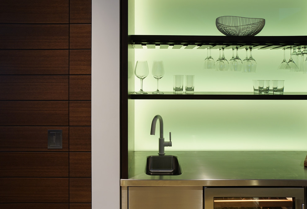 This is an example of a mid-sized contemporary single-wall wet bar in New York with open cabinets, dark wood cabinets, stainless steel benchtops, green splashback and grey benchtop.