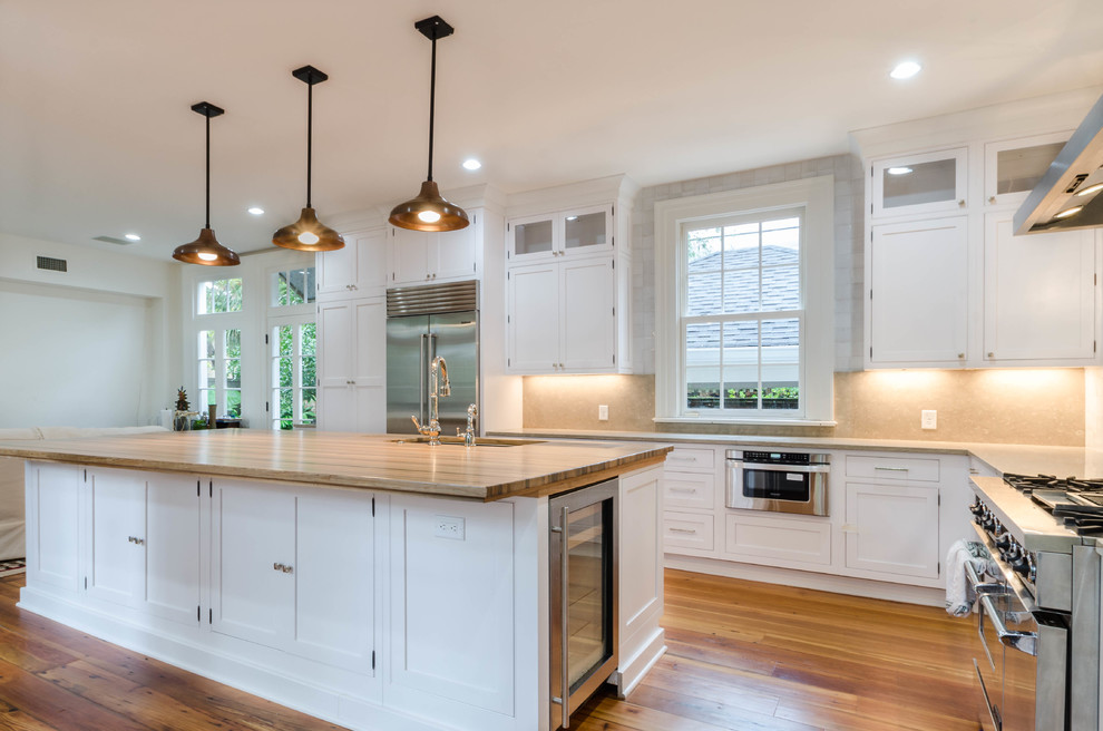 Design ideas for a mid-sized transitional l-shaped open plan kitchen in New Orleans with an undermount sink, flat-panel cabinets, white cabinets, wood benchtops, white splashback, medium hardwood floors and with island.
