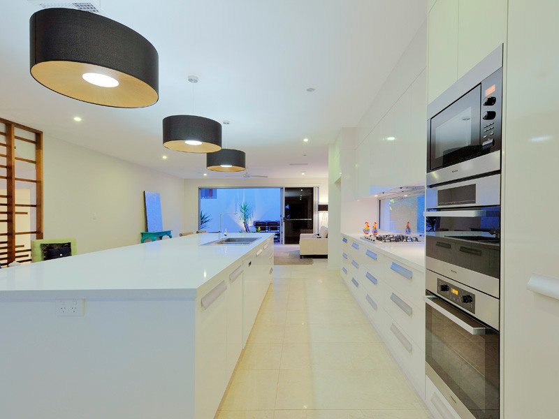 Inspiration for an expansive contemporary galley open plan kitchen in Brisbane with a double-bowl sink, white cabinets, quartz benchtops, window splashback, stainless steel appliances, ceramic floors, with island, white floor and white benchtop.