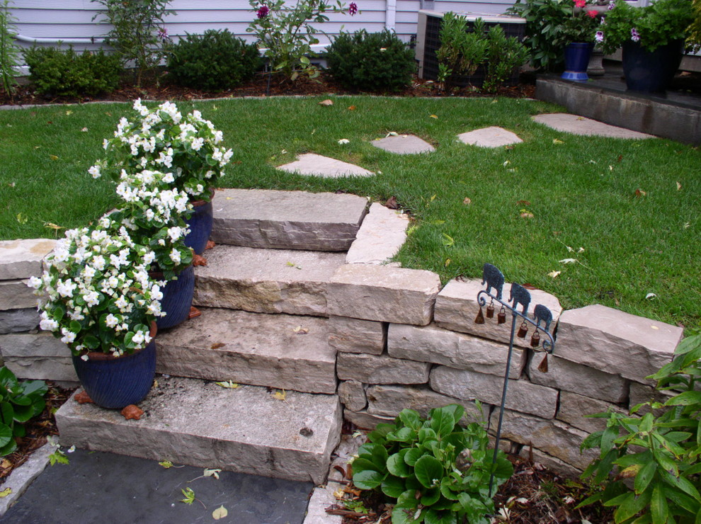 Photo of a large traditional backyard full sun formal garden for summer in Minneapolis with a retaining wall and natural stone pavers.