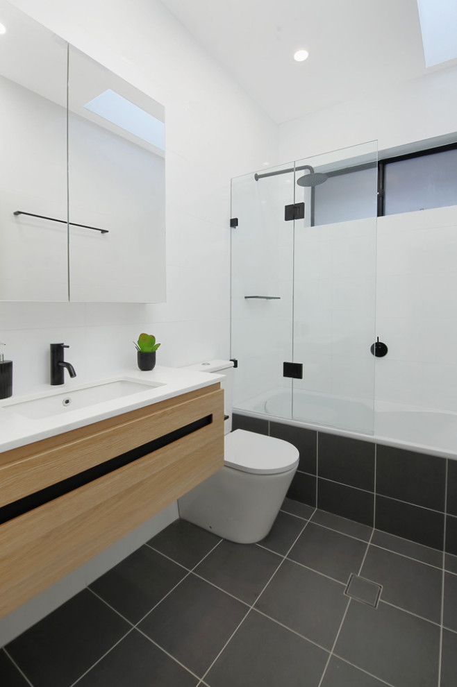 This is an example of a small contemporary kids bathroom in Sydney with recessed-panel cabinets, beige cabinets, an alcove tub, a shower/bathtub combo, a two-piece toilet, beige tile, ceramic tile, white walls, ceramic floors, an integrated sink, engineered quartz benchtops, beige floor, a hinged shower door and white benchtops.