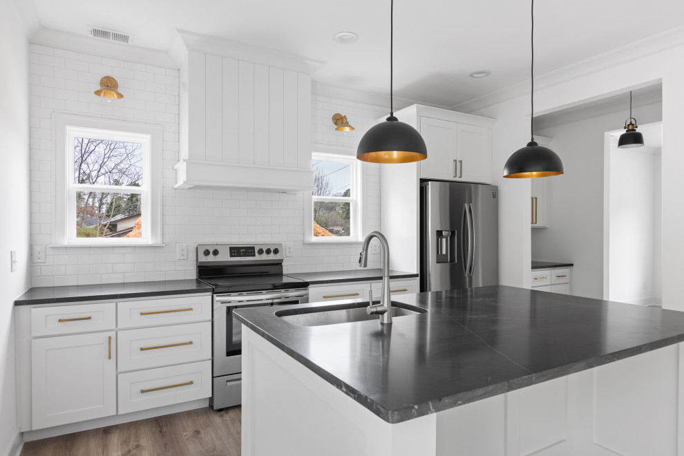 This is an example of a mid-sized transitional single-wall open plan kitchen in Other with an undermount sink, shaker cabinets, white cabinets, granite benchtops, white splashback, subway tile splashback, stainless steel appliances, vinyl floors, with island, brown floor and black benchtop.