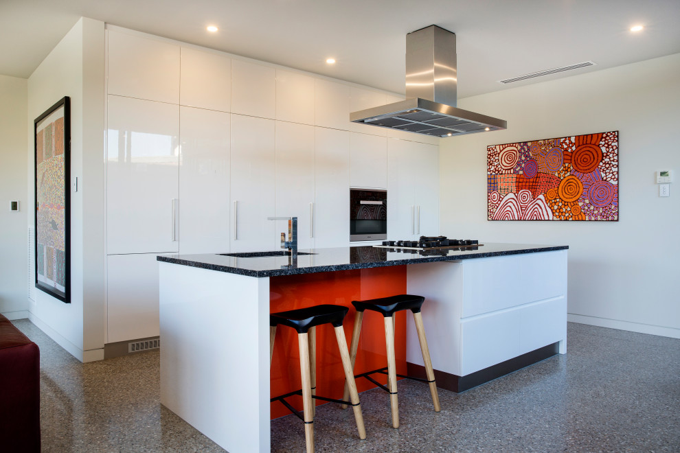 Photo of a mid-sized contemporary galley open plan kitchen in Adelaide with an undermount sink, flat-panel cabinets, white cabinets, granite benchtops, stainless steel appliances, concrete floors, with island, black benchtop and grey floor.