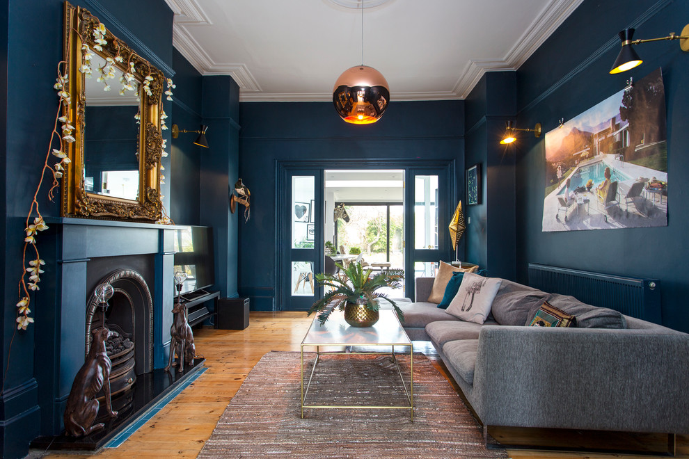 Mid-sized eclectic formal enclosed living room in London with blue walls, light hardwood floors, a standard fireplace, a metal fireplace surround, a freestanding tv and beige floor.