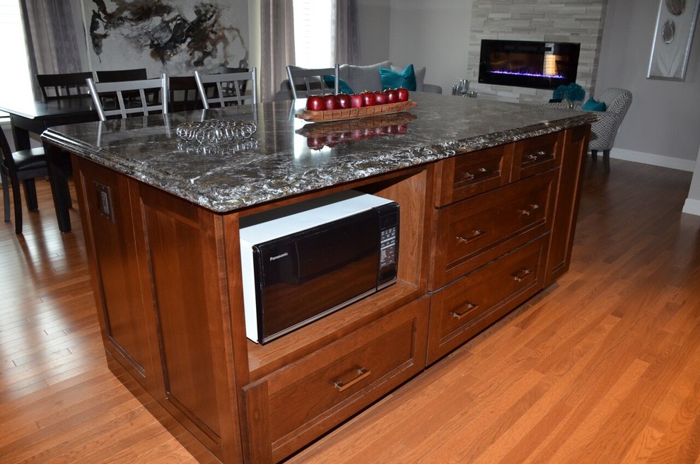 Large transitional l-shaped medium tone wood floor open concept kitchen photo in Toronto with an undermount sink, recessed-panel cabinets, dark wood cabinets, quartzite countertops, gray backsplash, glass tile backsplash, stainless steel appliances and an island
