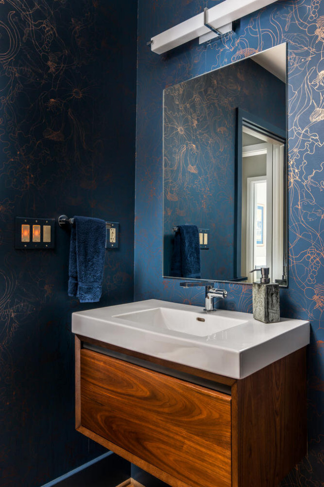 Contemporary powder room in Nashville with flat-panel cabinets, medium wood cabinets, black tile, blue walls, a console sink, brown floor, white benchtops, a floating vanity and wallpaper.