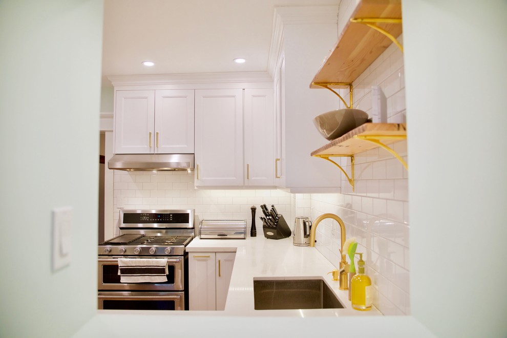 This is an example of a small contemporary u-shaped separate kitchen in Toronto with an undermount sink, shaker cabinets, white cabinets, quartz benchtops, white splashback, ceramic splashback, stainless steel appliances, medium hardwood floors, brown floor and white benchtop.