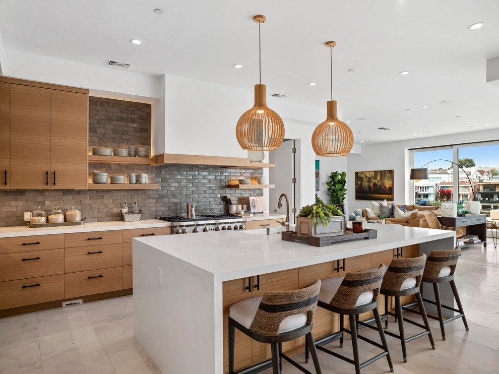 This is an example of a contemporary galley open plan kitchen in Orange County with a farmhouse sink, flat-panel cabinets, medium wood cabinets, grey splashback, stainless steel appliances, with island, beige floor and white benchtop.