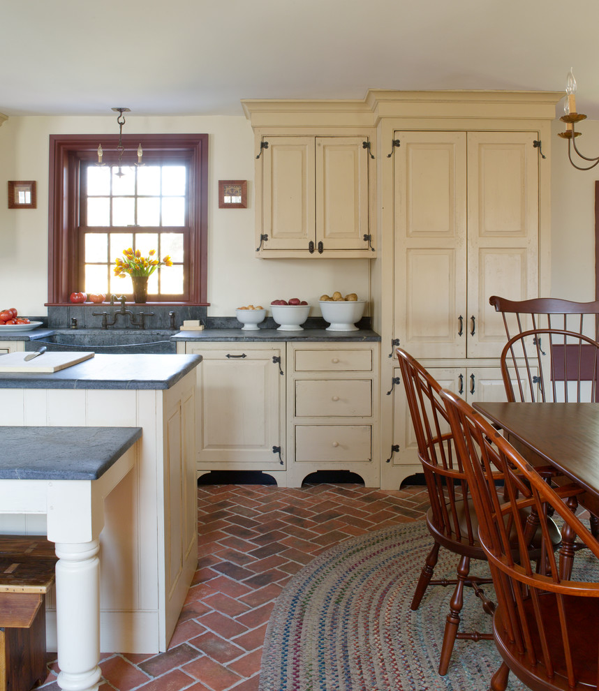 Mid-sized country single-wall eat-in kitchen in Philadelphia with a farmhouse sink, raised-panel cabinets, with island, brick floors, beige cabinets, concrete benchtops, panelled appliances, red floor and grey benchtop.