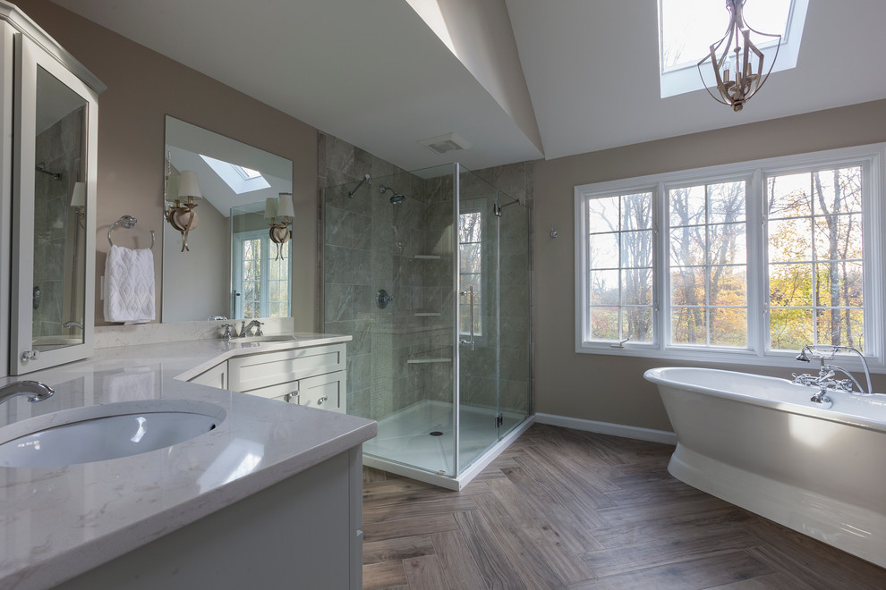 Inspiration for a mid-sized transitional master gray tile and porcelain tile porcelain tile and gray floor freestanding bathtub remodel in New York with flat-panel cabinets, gray cabinets, a two-piece toilet, gray walls, an undermount sink, quartz countertops and a hinged shower door