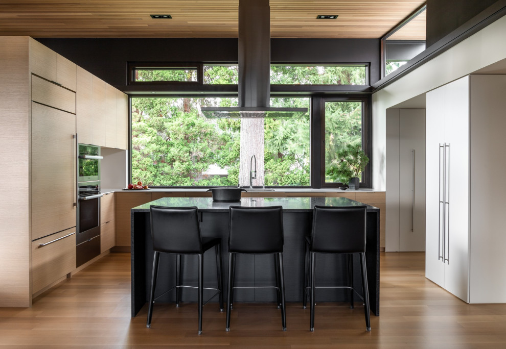 Inspiration for a contemporary l-shaped open plan kitchen in Seattle with an undermount sink, flat-panel cabinets, light wood cabinets, white splashback, stainless steel appliances, medium hardwood floors, with island, white benchtop and wood.